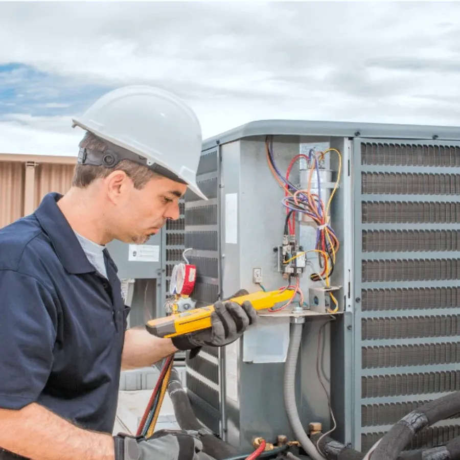 HVAC technician in a hard hat testing an outdoor air conditioner with a multimeter
